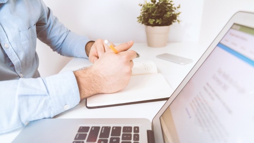 Man writing in notebook next to laptop