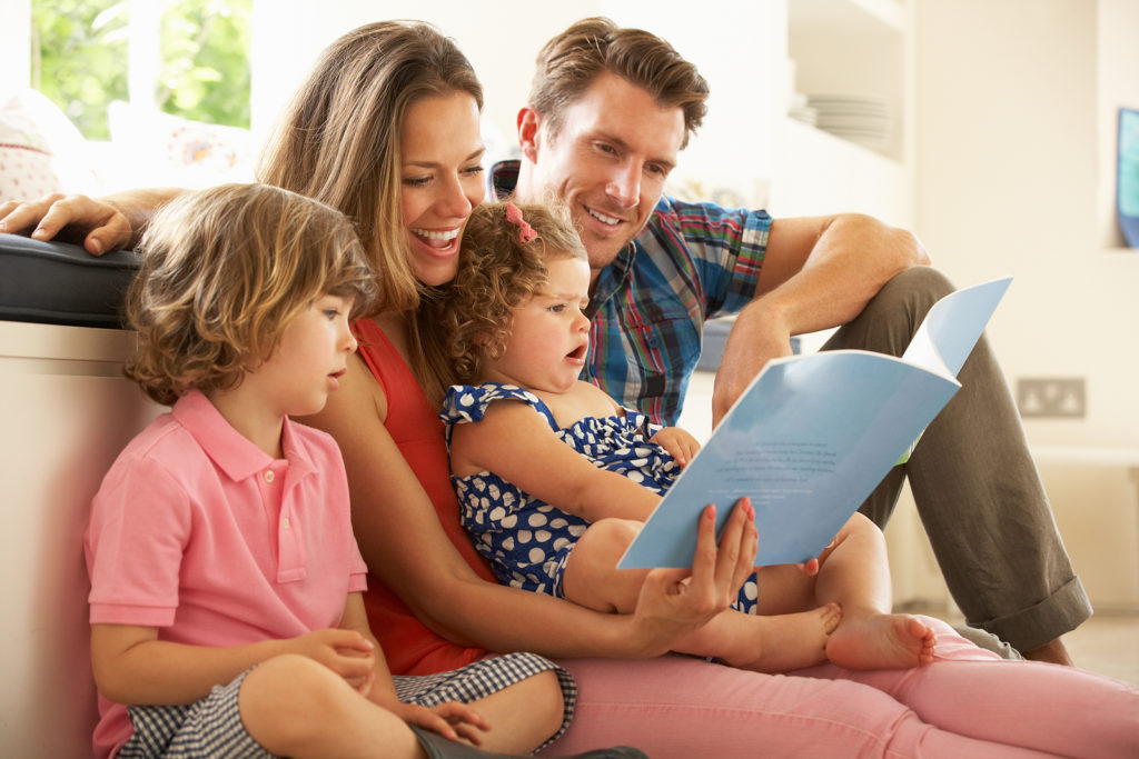 Two white parents reading to their two children.